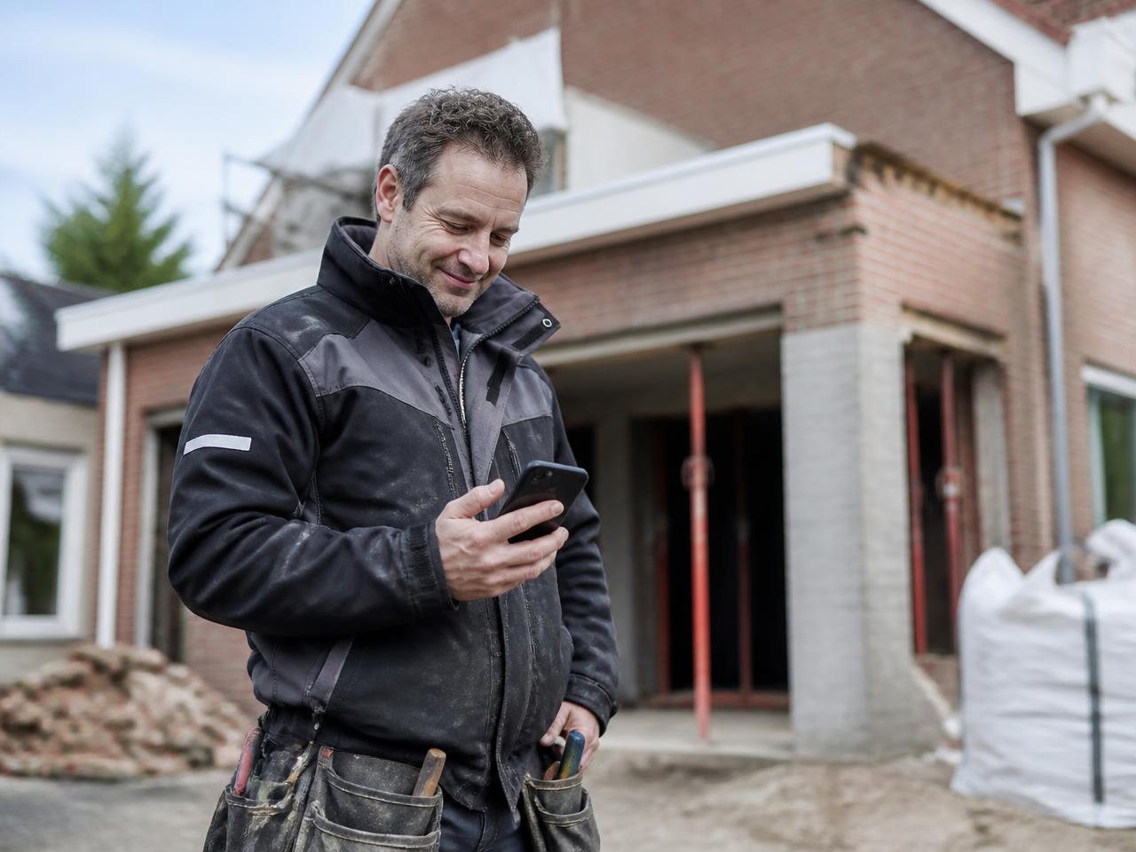 Vakman op de werf leest een nieuwe offerteaanvraag op zijn smartphone